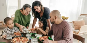 Family gathering around dinner table eating pizza